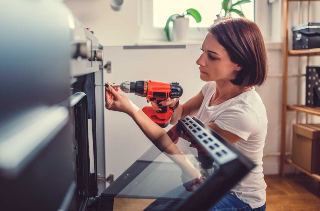 Consigli per la manutenzione della casa - Donna che fa riparazioni in cucina usando trapano.